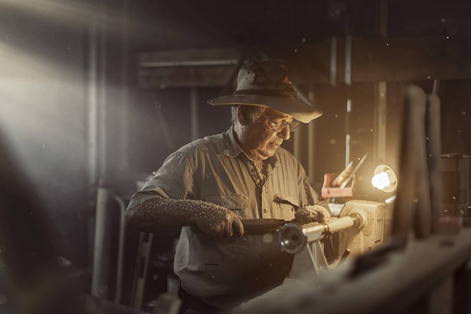 Creative photography projects by Dale Travers Photography. Image shows master carpenter at work with moody lighting and woodchips flying through the air.